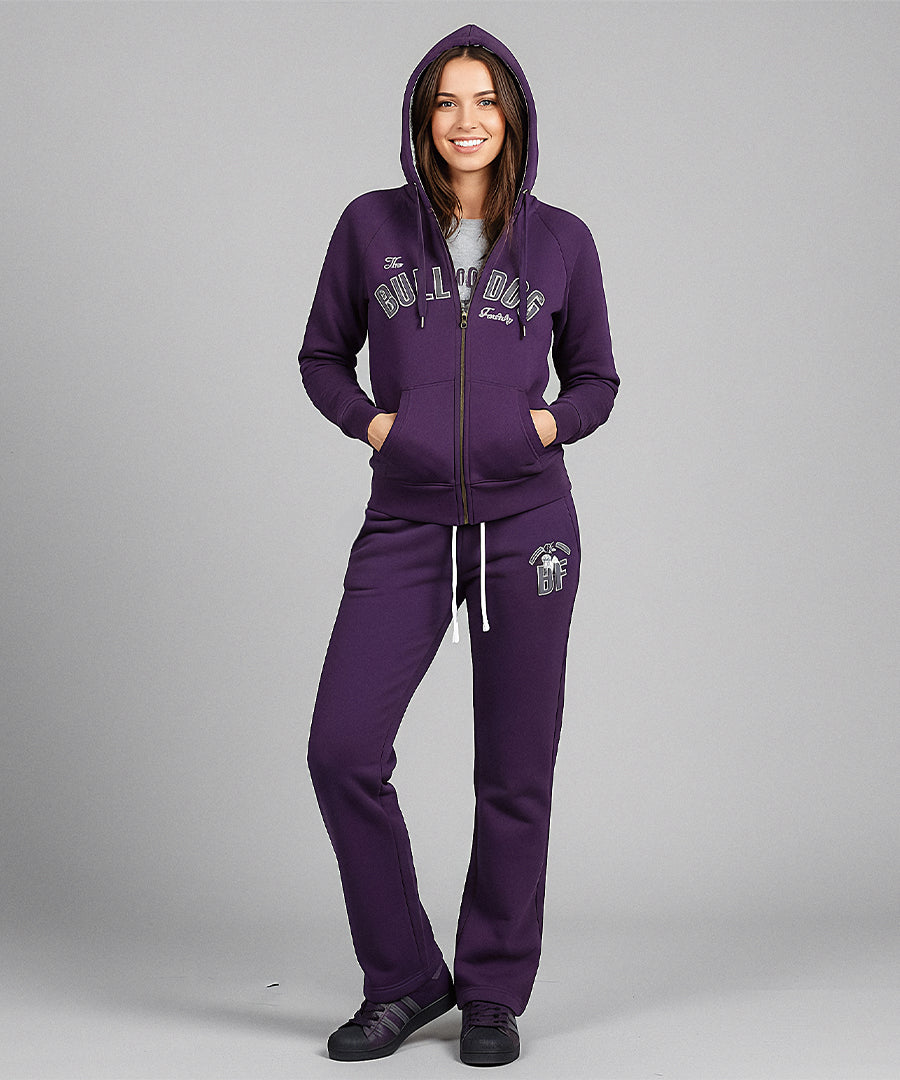 Woman wearing a purple tracksuit with a brand logo on a gray background